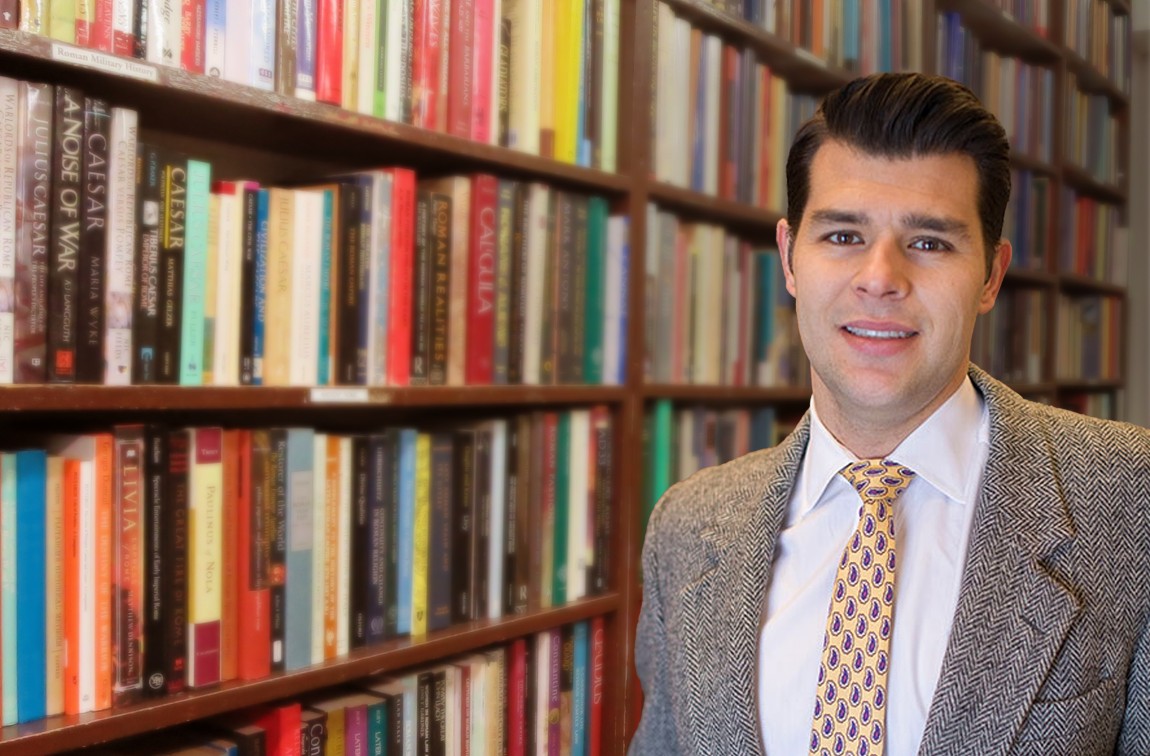 A man stands in front of a colorful bookshelf.